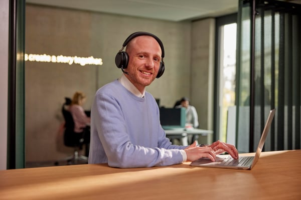 netgo Mitarbeitender mit Headset und Laptop schaut lächelnd in die Kamera